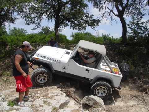 1973 Ford Bronco - Jeep Wrangler navigating a challenging off-road course with rocky terrain and trees.