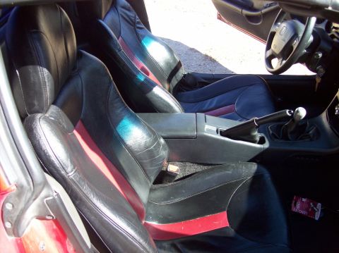 1989 Ford Bronco - The interior of a car is shown, black seats with red and blue stripes, a center console, and a steering wheel.
