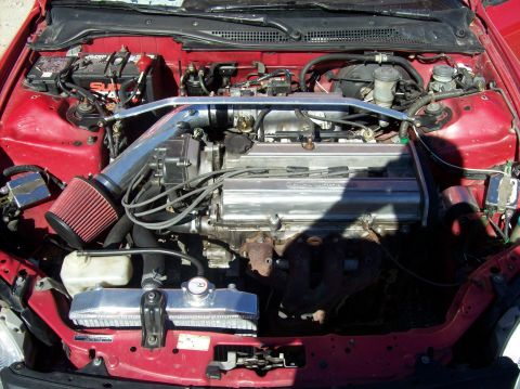 1989 Ford Bronco - The engine bay of a red car features an aftermarket cold air intake and a shiny aluminum radiator.