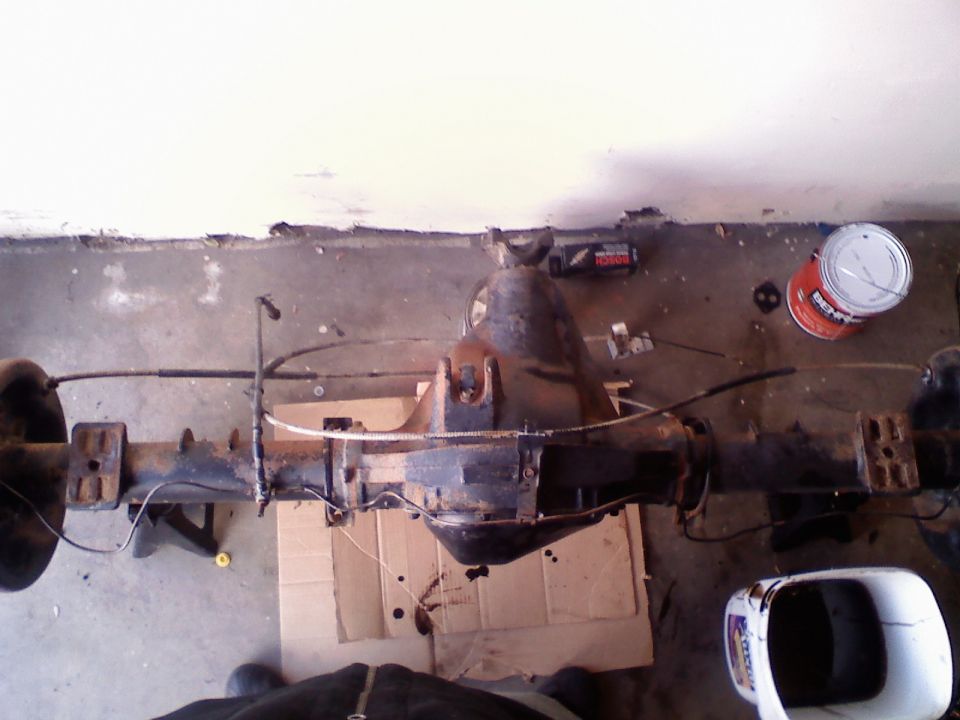 Rear axle assembly with differential housing, brake lines, and U-bolts, resting on cardboard