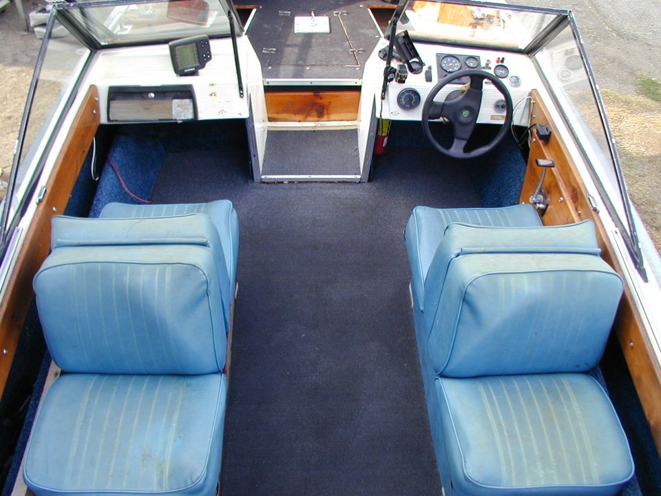 Boat interior with blue vinyl seats, dark carpet, and a steering wheel