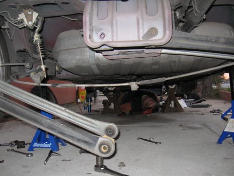 1989 Ford Taurus - Mechanic works on the undercarriage of a vehicle, with the fuel tank and suspension parts visible.