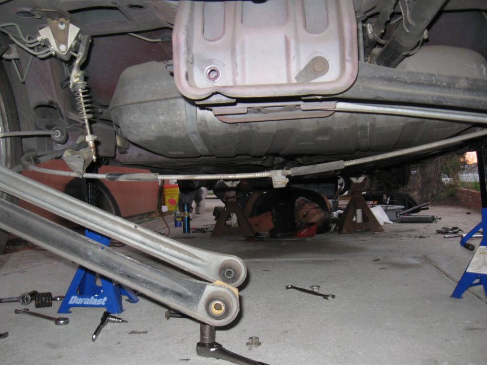 Underbody view of a car with a mechanic working, showing fuel tank and suspension components