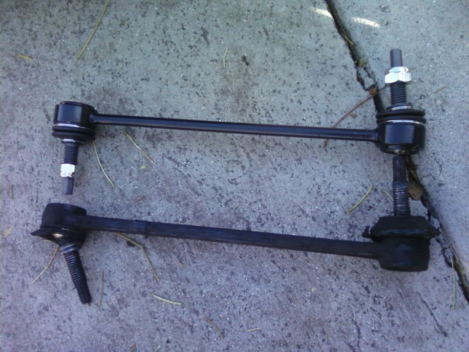 Two car suspension stabilizer links laid out on concrete. One is new, the other looks used