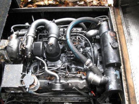 2000 Ford E350 - Overhead view down into an engine compartment showing a grimy inline diesel engine with cast intake elbows, injection lines, a blue reinfor…