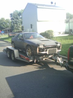 1987 Mazda RX-7 - A dark coupe is transported on a trailer, its front bumper removed to reveal an intercooler.