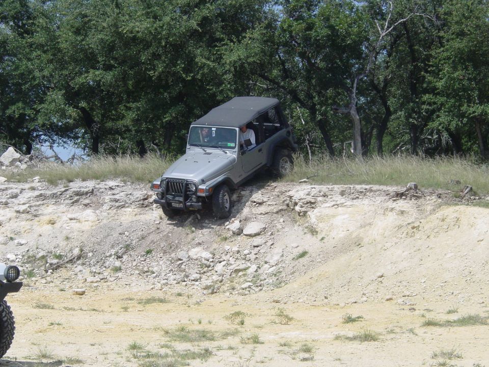 Silver Jeep Wrangler driving off-road on a rocky incline