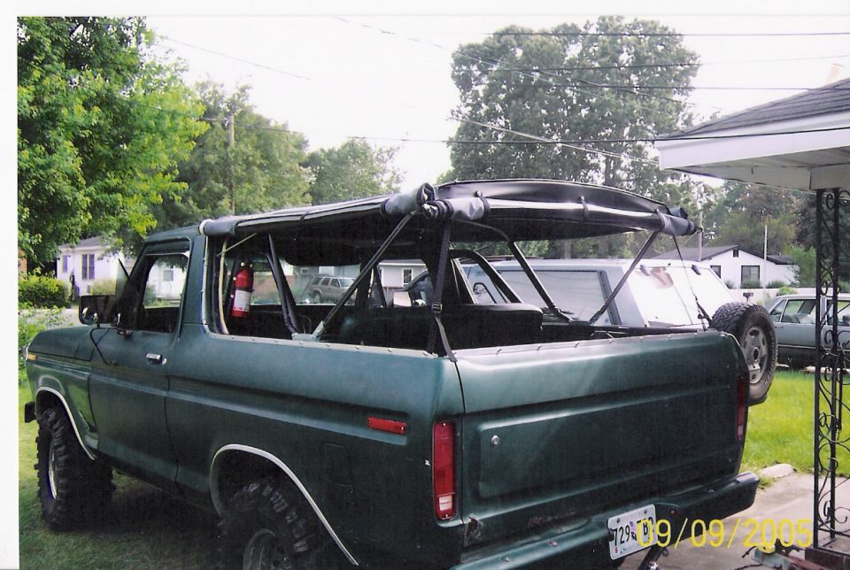 Green SUV with a soft top frame, spare tire on the back, and another vehicle parked behind it