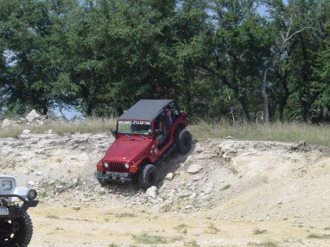 1973 Ford Bronco - A red Jeep Wrangler navigates a challenging rocky terrain, with another vehicle visible to the left.
