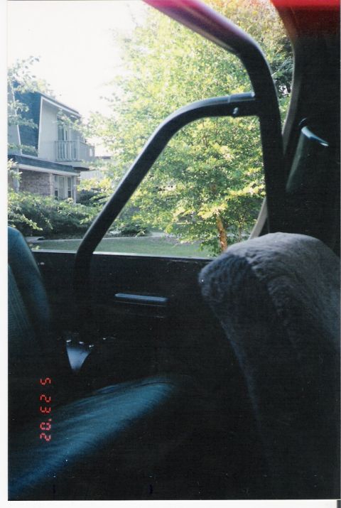 1979 Ford Bronco - View from inside a vehicle shows a residential house and trees through the window.