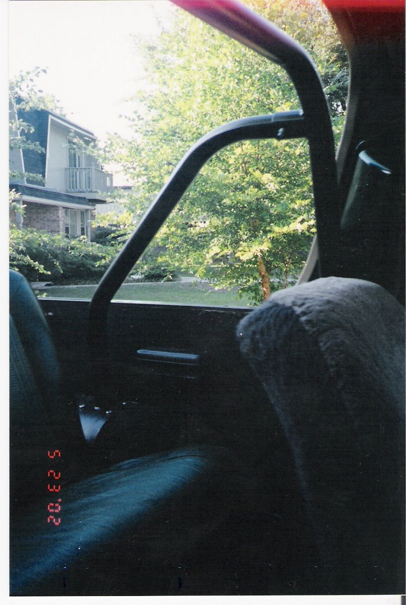 Interior shot looking out passenger window, shows seat, roll bar, and trees outside