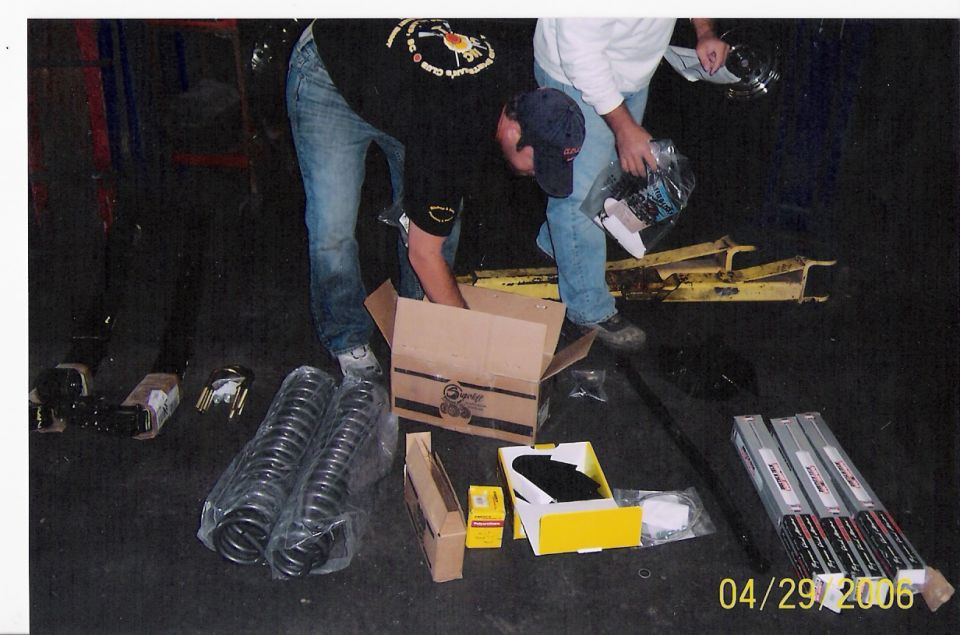 Two people unpack car parts including coil springs and boxed components