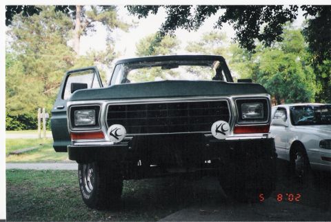 1979 Ford Bronco - This green SUV, possibly a 1979 Ford Bronco, is parked outside with its door ajar. Another vehicle is visible to the right.