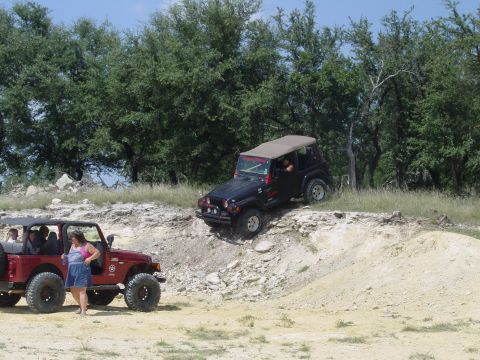 1973 Ford Bronco - Two Jeeps navigate a challenging off-road course with trees in the background.