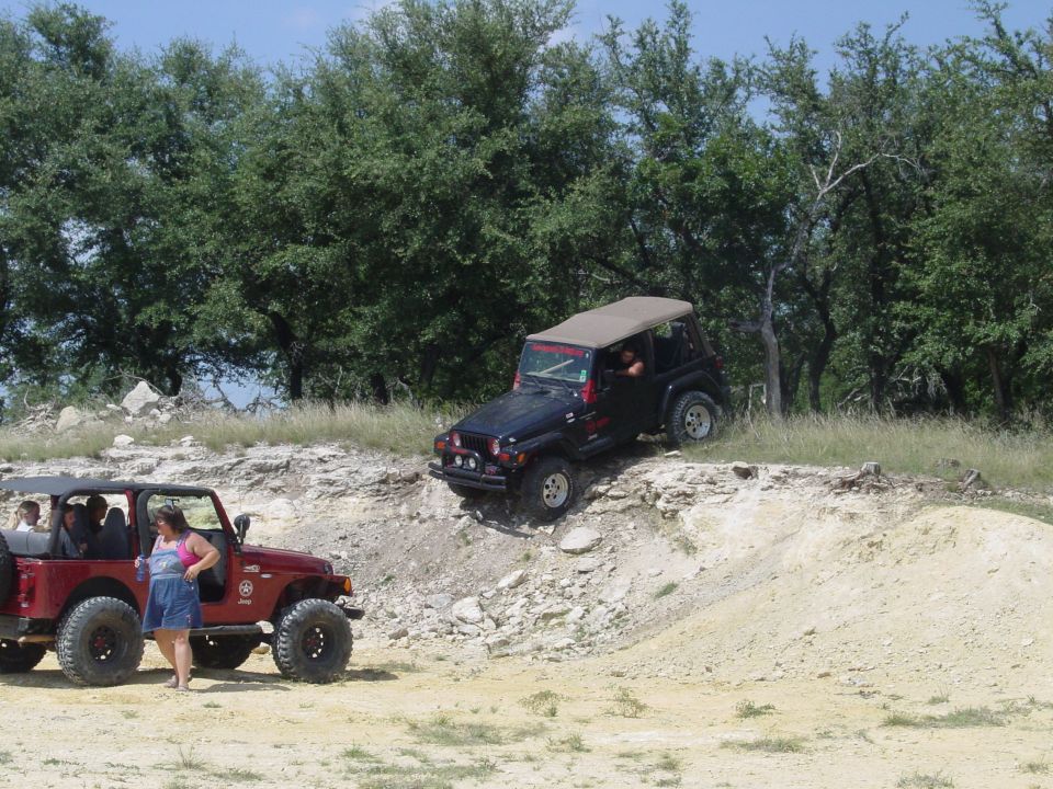 Red Jeep parked on dirt, black Jeep climbing a rocky incline