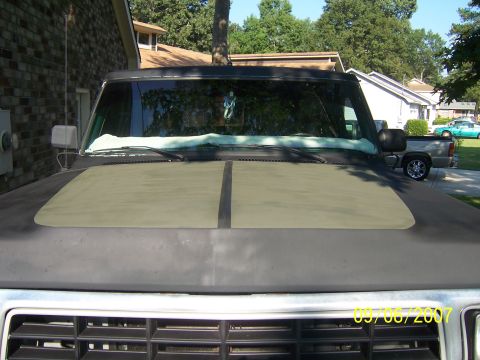 1979 Ford Bronco - The hood of a dark SUV features a contrasting olive green panel, with another truck visible in the background.