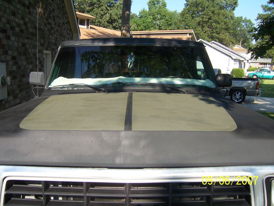 Dark SUV hood with olive green panel. Another truck visible