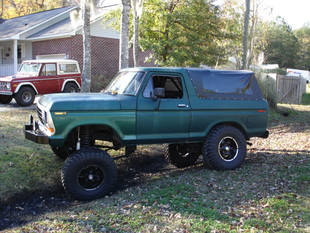 Lifted green Ford Bronco with soft top parked next to a red Ford Bronco