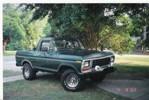 1979 Ford Bronco - This green Ford Bronco is parked on a driveway with trees and grass in the background.