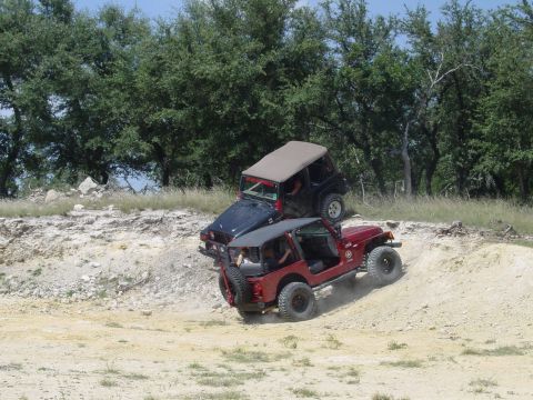 1973 Ford Bronco - Two Jeeps navigate a challenging off-road course with wooded hills in the background.