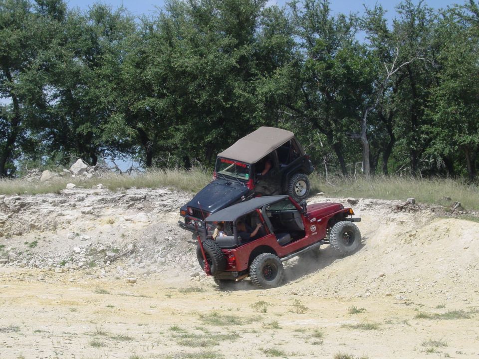 Red Jeep climbing a dirt hill with a black Jeep on top of it