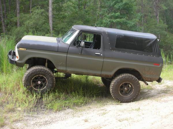 Olive green and black 1978 Ford Bronco with a soft top, lifted suspension, and off-road tires on a dirt path