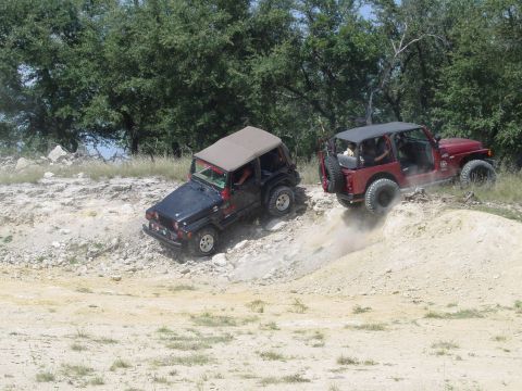 1973 Ford Bronco - Two Jeeps tackle a challenging off-road course, kicking up dust as they climb.