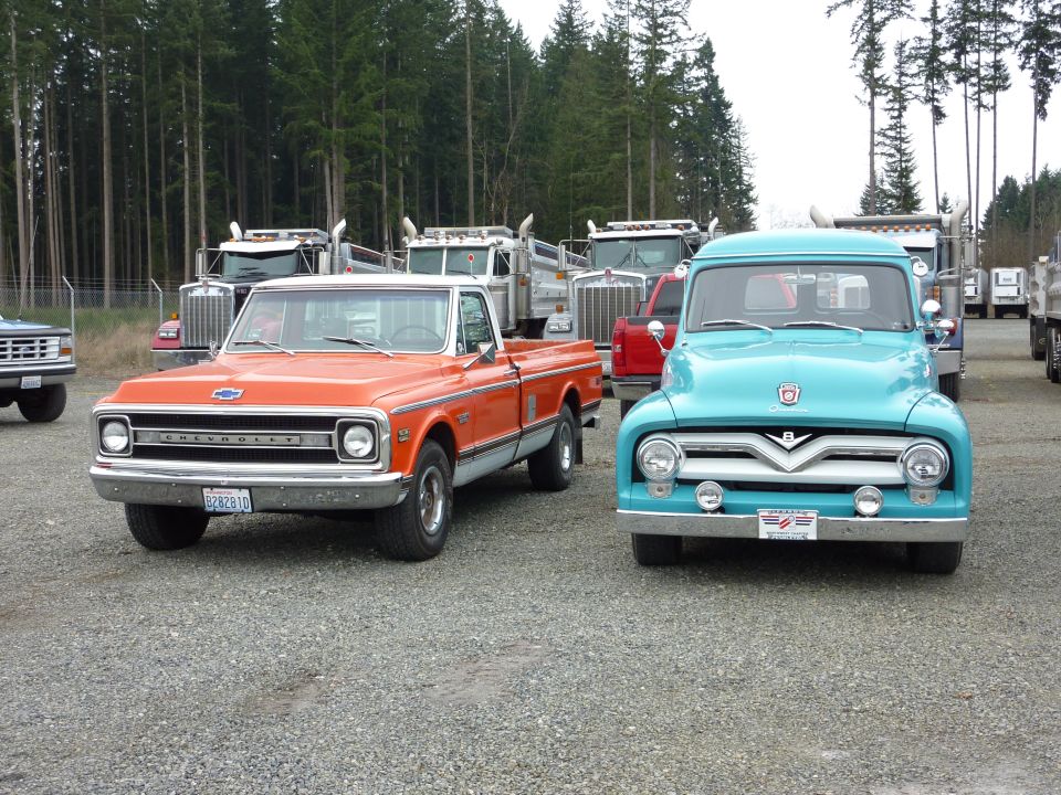 Front view of an orange Chevrolet pickup and a turquoise Ford pickup parked on gravel
