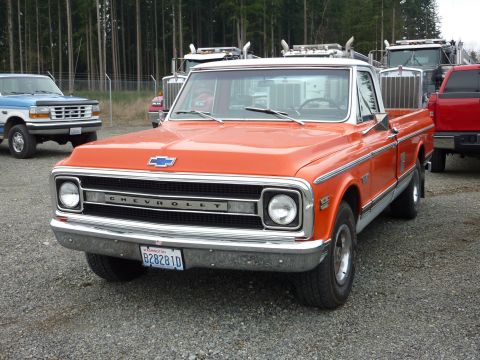 1981 Kenworth W900A - This orange Chevrolet pickup truck is parked in a lot with other vehicles visible in the background.
