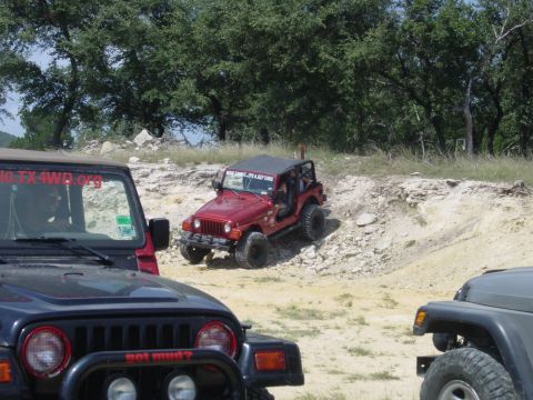1973 Ford Bronco - Multiple Jeeps navigate a challenging off-road course on a sunny day.