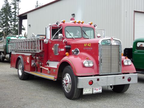 1981 Kenworth W900A - A red fire truck with the number 42 prominently displayed on its side is parked next to a green pickup truck.