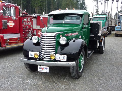1981 Kenworth W900A - A 1940 GMC flatbed truck is parked next to a red fire truck and other trucks.