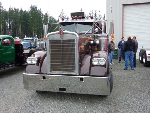 1981 Kenworth W900A - A brown Kenworth semi-truck is parked outside a building with other trucks visible.