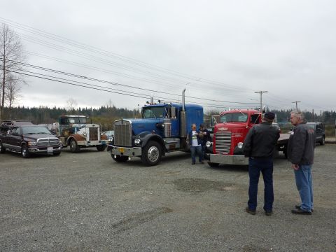 1981 Kenworth W900A - Several trucks are gathered in a gravel lot under an overcast sky, with a few people observing them.