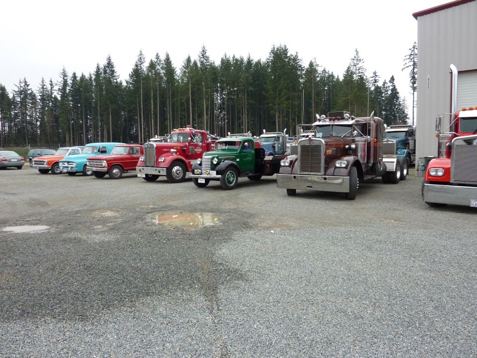 Several old trucks parked in a lot, including a red fire truck, a green truck, and a brown semi-truck
