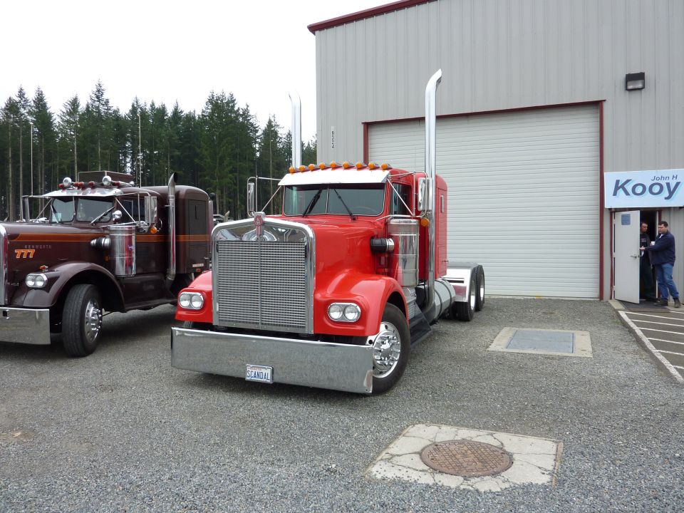 Red 1981 Kenworth W900A semi-truck, 3q-front view, parked next to a brown truck