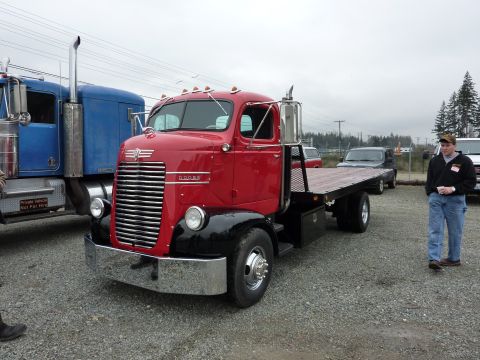 1981 Kenworth W900A - A classic red flatbed truck is parked next to a blue semi-truck, with a man standing nearby.