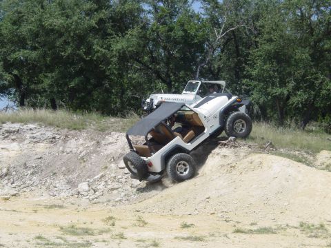 1973 Ford Bronco - Two Jeeps navigate a steep, sandy incline on a wooded trail.