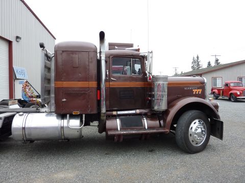 1981 Kenworth W900A - Side view of a brown Kenworth 777 semi-truck parked outdoors with a red pickup in the background.