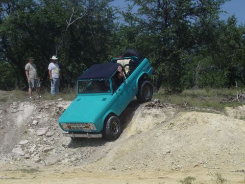 1973 Ford Bronco - A teal Ford Bronco navigates an off-road trail with two onlookers.