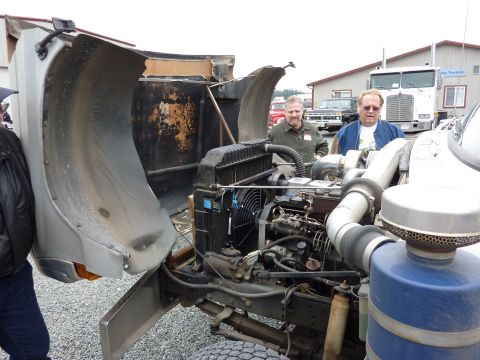 1981 Kenworth W900A - Two men examine the engine of a truck with its hood open, revealing the complex machinery within.