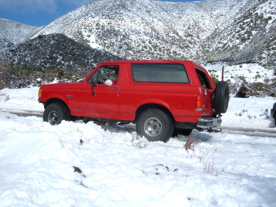 Red Ford Bronco in profile parked in snow with rear tire carrier and chrome wheels