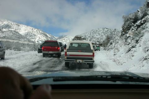 1991 Ford Bronco - Vehicles are stuck in traffic on a snow-covered mountain road with steep, rocky slopes.
