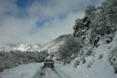 1991 Ford Bronco - A white and red pickup truck navigates a snow-covered mountain road under a cloudy sky.
