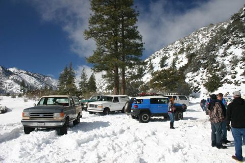 1991 Ford Bronco - A gray 1991 Ford Bronco is parked in the snow with other vehicles nearby under a bright blue sky.