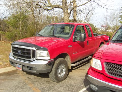 2007 Ford Mustang - A red Ford F-250 Super Duty truck is parked outdoors next to another red vehicle.