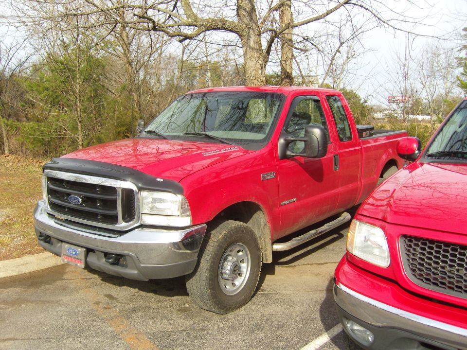 Red Ford F-250 Super Duty truck, 3/4 front view, parked next to another red vehicle