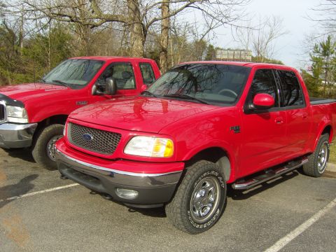 2007 Ford Mustang - A red Ford F-150 pickup truck is parked next to another red truck, with the front of the F-150 prominently displayed.