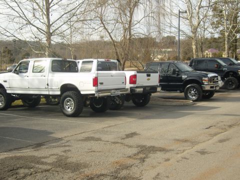 2007 Ford Mustang - Multiple lifted pickup trucks are parked in a lot on a cloudy day.
