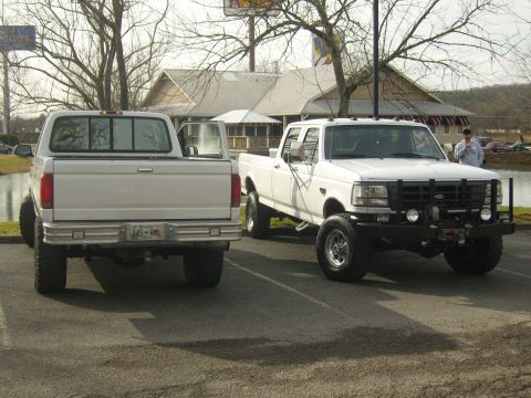 2007 Ford Mustang - Two white Ford pickup trucks parked in a lot. The truck on the right is a 1992 model with a custom grille guard.